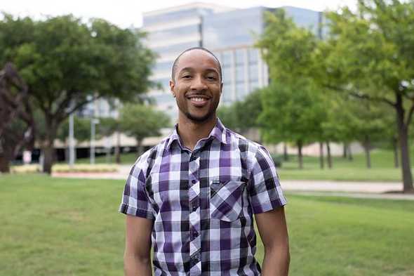 Man smiling in front of trees and building